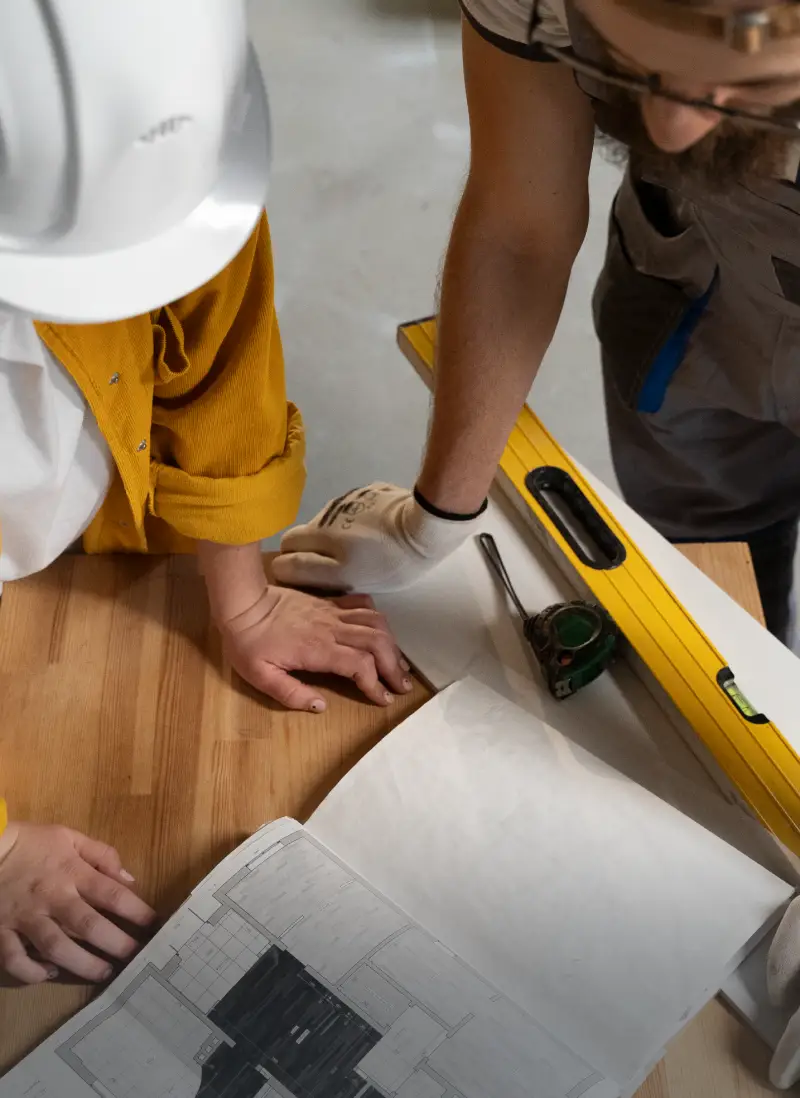 Contractors reviewing floor plan beside level and measuring tape