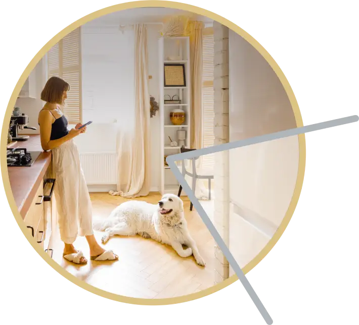 Young woman standing in a bright modern kitchen using her phone while a large white dog rests on the floor.